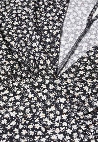 Tissu noir avec petit motif floral blanc et couture froncée près d'une encolure en V étroite avec bord de couture visible.