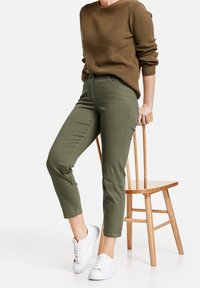 Olivgrön bomulls-chinos med slim fit, sidfickor och normal hög midja, parat med en brun strukturerad tröja och vita sneakers.