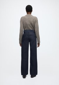 Temno modri široki kavbojki iz jeansa, z visokim pasom, dvema zadnjima žepoma in minimalističnim dizajnom. Na vrhu je teksturiran siv pulover.