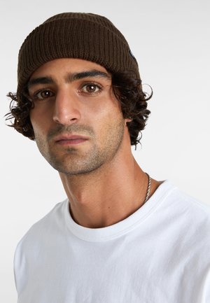 Gorro marrón de canalé con un ajuste ceñido, hecho de material de punto, llevado por una persona con una camiseta blanca, que presenta una sutil cadena metálica.