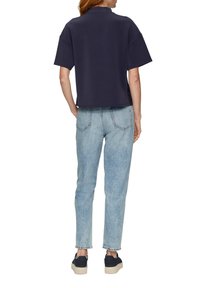 Marineblaues, kurzärmeliges Poloshirt, kombiniert mit hellblauen Jeans. Die Sneakers haben eine strukturierte Sohle. Schlichtes, sauberes Design.