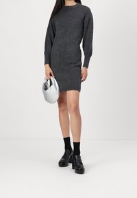 Robe pull grise tricotée à manches longues, avec poignets et ourlet côtelés, assortie à des chaussures à plateforme noires et un sac à main métallique argenté.