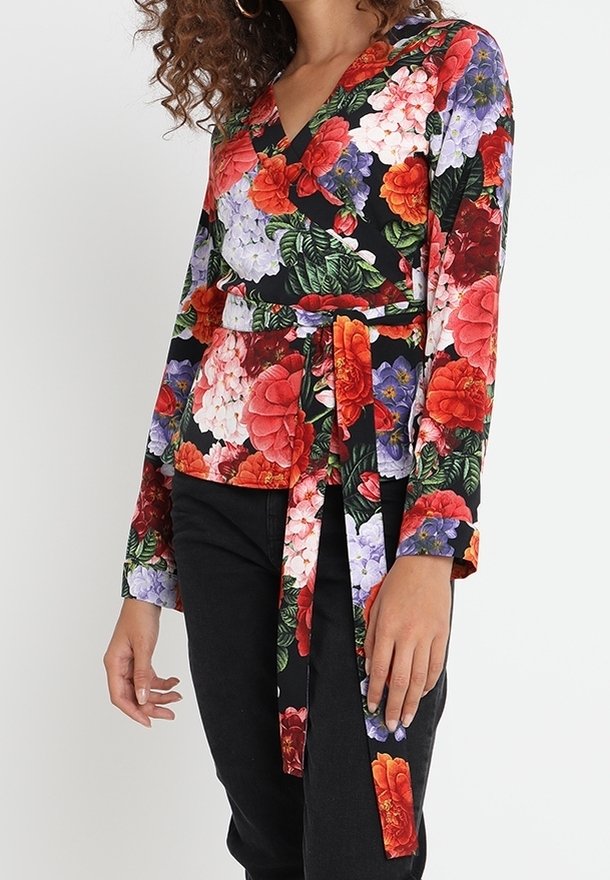 Haut portefeuille floral noir avec des fleurs rouges, violettes et blanches, agrémenté de feuilles vertes. Manches longues et détail de ceinture nouée.