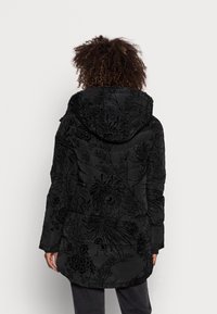 Svart vadderad jacka med ett blommönster i en glänsande finish, med huva och sidofickor, strukturerad med horisontell sömnad.