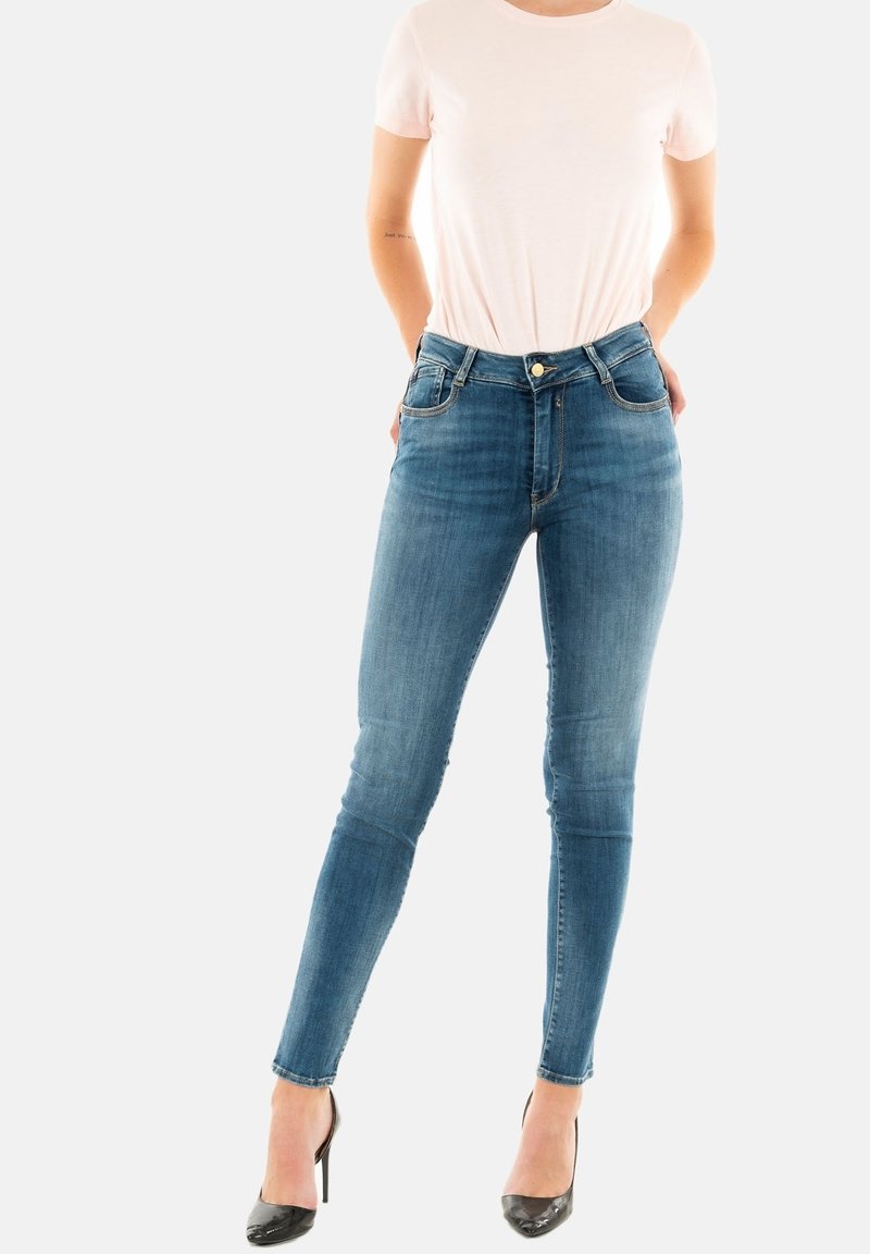 Blauwe denim skinny jeans met een hoge taille, lichte vervaging en twee voorzakken. Gecombineerd met een lichtroze t-shirt met korte mouwen en zwarte hakken.