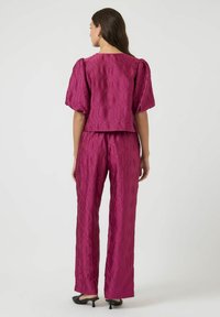 Fuksjowy zestaw składający się z krótkiego topu i spodni z szerokimi nogawkami, z falistą fakturą, krótkimi bufkami oraz gładkim materiałem o błyszczącym wykończeniu.