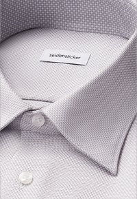 Lichtgrijs shirt met een structuurstof en een houndstooth patroon, klassieke kraag en witte knopen. Etiket zichtbaar in de kraag.