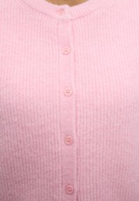Μαλακή ροζ πλεκτή ζακέτα με ριμπ ύφανση και έξι ταιριαστά ροζ κουμπιά μπροστά.