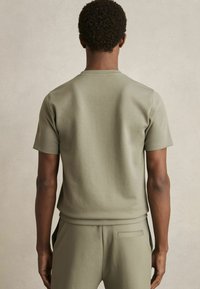 Olíva zöld, rövid ujjú pulóver, puha pamut anyagból, laza fazon, kerek nyakkivágással, hátulról bemutatva, sima textúra, minimalista design.