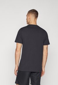 T-shirt nera a maniche corte, collo rotondo, realizzata in cotone morbido, con orlo dritto e design minimal. Indossata con pantaloni corti neri.