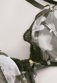 Grøn blomsterblonde-bh med gennemsigtigt mesh-materiale, blomsterprint, detaljeret blondetrim og guldfarvede metaldele. Justerbare stropper inkluderet.