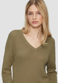 Maglione a maglia verde oliva con scollatura a V, motivo testurizzato e maniche lunghe, caratterizzato da dettagli a costine al colletto e ai polsini.