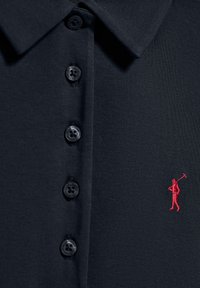 Navyblå pikétröja i texturerad tyg med krage, utrustad med svarta knappar och en liten röd broderad golfspelare-logotyp.