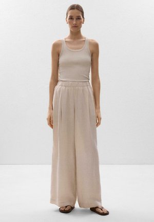 Bézs színű ujjatlan felső és bő, világos bézs színű, rugalmas derékpántos nadrág. A ruházat laza kialakítású és minimális textúrával rendelkezik.