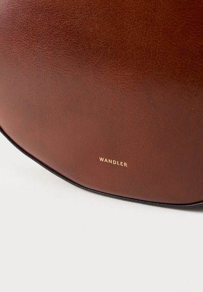 Geantă de mână din piele maro, cu textură netedă, formă rotunjită și inscripționare aurie. Marginile au o bordură neagră contrastantă.