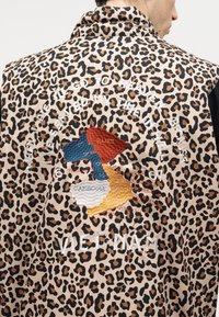 Chaqueta de estampado de leopardo con un mapa bordado de Vietnam, Camboya y Laos, rodeado de texto blanco y "VIET NAM" en la parte inferior.