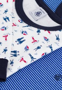 Vêtement en coton avec un fond blanc présentant des motifs nautiques en rouge et bleu, accompagné de tissu rayé bleu et blanc. Finition marine.