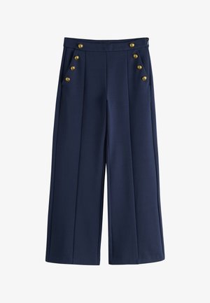 Tmavomodré nohavice širokého strihu s vysokým pásom a dvoma radmi po šesť zlatých gombíkov na predných vreckách.
