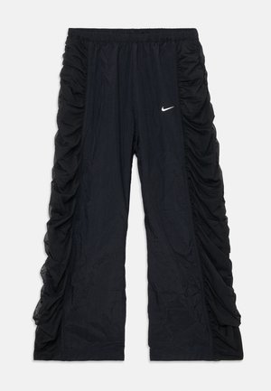 Pantalons de sport noirs avec des détails froncés sur les côtés, une taille élastique et un petit logo Nike blanc à l'avant. Tissu léger.
