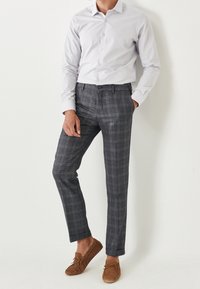 Szare spodnie w kratę o dopasowanym kroju, zestawione z jasnoszarym, zapinanym na guziki shirt'em. Całość uzupełniają brązowe zamszowe loafersy.