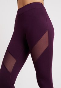 Fioletowe legginsy z wysokim stanem, z siateczkowymi wycięciami w geometryczny wzór. Wykonane z gładkiego, elastycznego materiału dla wygody.