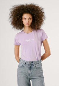 Gaiši violetas īsām piedurknēm T-krekls ar "Pepe Jeans London" logo baltā krāsā. Saskaņots ar gaiši ziliem augsta vidukļa džinsiem.