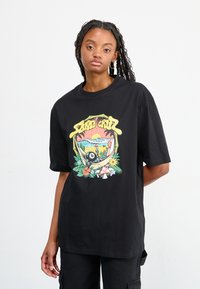 T-shirt in cotone nero con un design grafico colorato che presenta elementi tropicali, tra cui fiori, un fungo e una scena di spiaggia.