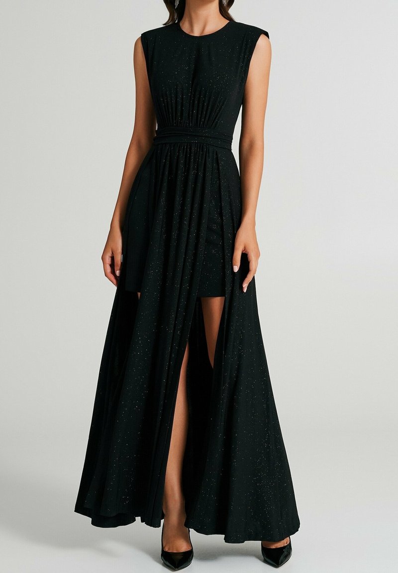 Robe de soirée noire sans manches avec paillettes, fente haute à l'avant dévoilant une jupe courte, portée avec des talons noirs pointus.