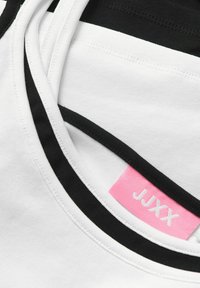 Gros plan sur un tissu rayé blanc et noir avec une étiquette de vêtement rose indiquant la marque JJXX à l'intérieur d'un col.