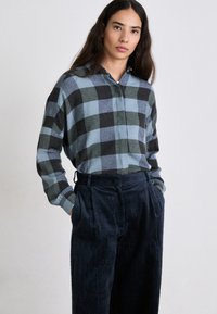 Checkered button-up shirt in blue and black tones; paired with dark corduroy trousers featuring a textured finish and side pockets.