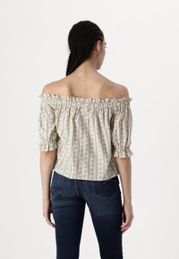 Off-the-shoulder bluse i kremfarge med blomster- og stripemønster, volanger på ermene og elastisk midje. Kombinert med mørke jeans.