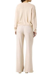 Beige Strickpullover mit lockerer Passform und geripptem Saum, kombiniert mit hellbeigen weit geschnittenen Hosen mit Gesäßtaschen und glatter Textur.