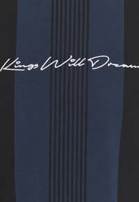 Blå och svart randig t-shirt med "Kings Will Dream" i vit broderad text på framsidan. Slät bomullstextur.