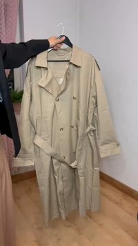 Trench coat bege com um design de duplo botão, grande colarinho, mangas longas e cinto amarrado na cintura. Feito de tecido leve.