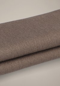 Dzianina w ciepłym kolorze taupe, prezentująca delikatną fakturę z równomiernie rozmieszczonymi oczkami, starannie złożona do ekspozycji.