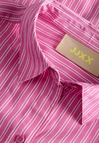 Lyserødstribet skjorte med hvide lodrette linjer, der har en fold-down krave, knaplukning og et mærke mærket "JJXX" i gult.