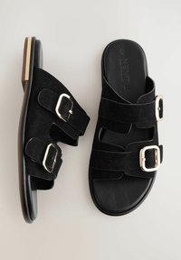 Schwarze Wildledersandalen mit zwei verstellbaren Riemen und goldfarbigen Schnallen, ausgestattet mit einer glatten schwarzen Fußbett und einer strukturierten braunen Sohle.