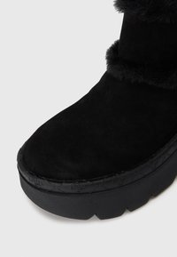 Melnas zamša ziemas kurpes ar pēdas odziņu un biezu teksturētu gumijas zoli, tuvplāns uz pirksta un sānu detaļām.