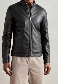 Schwarze Lederjacke mit Stehkragen, Frontreißverschluss und zwei Seitentaschen. Glatte Textur und taillierte Passform.