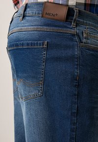 Džínové kalhoty v tmavě modré barvě, s texturovaným povrchem, oranžovým prošitím a koženou nášivkou MEN+ na pase, s klasickými zadními kapsami.