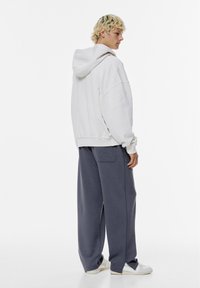 Overmaatse lichtgrijze hoodie met een kontzak en een capuchon met trekkoord, gecombineerd met loszittende donkergrijze joggingbroek met een achterzak.