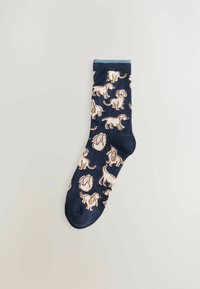 Marinblå strumpor i bomull med ljusbeiga hundmönster. Designen inkluderar olika hundpositioner, med ribbad klack och mjuk textur.