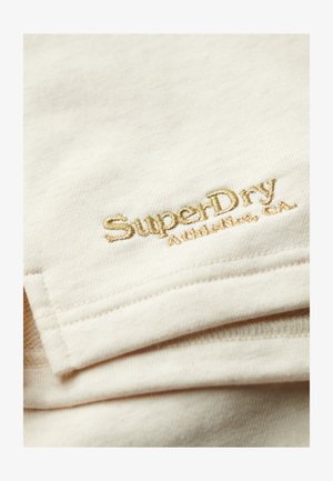 Elfenbenfarvet stof med en blød tekstur, der har prægede gyldne sting med "SuperDry" og "Athletic, CA" i nederste højre hjørne.