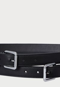 Mustaa nahkavyötä sileällä pinnalla. Varustettu hopeisella metallisoljella ja useilla reikiä koon säätämiseksi. Yksinkertainen muotoilu.