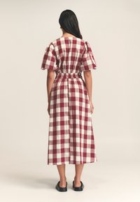 Sukienka w kratkę w kolorze bordowym i białym, z bufiastymi rękawami, z wciągniętą talią i swobodnym długością, wykonana z lekkiej, teksturowanej tkaniny.