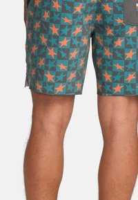 Pantaloni corti colorati con un motivo di stelle arancioni e teal su uno sfondo grigio, realizzati in un tessuto morbido e con un dettaglio di tasca laterale.