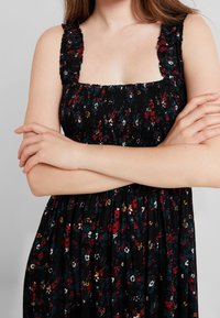 Robe noire à fleurs avec corsage froncé, bretelles volantées, ornée de motifs floraux multicolores. Tissu fluide avec une coupe décontractée.