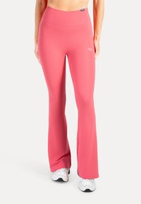 Roze uitlopende sportlegging met een hoge tailleband, een gladde textuur en logodetail aan de zijkant. Gecombineerd met witte sneakers.