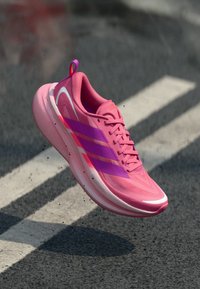 Pink athletic shoe with a streamlined design, featuring a smooth upper, light cushioning, and three parallel purple stripes.