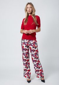 Top de punto rojo acanalado de manga corta combinado con pantalones de pierna ancha blancos con flores que presentan patrones rojos y morados y acentos negros. Tacones negros.